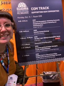 Selfie of Erika standing next to the schedule for the day she presented. She is smiling and looking at the camera